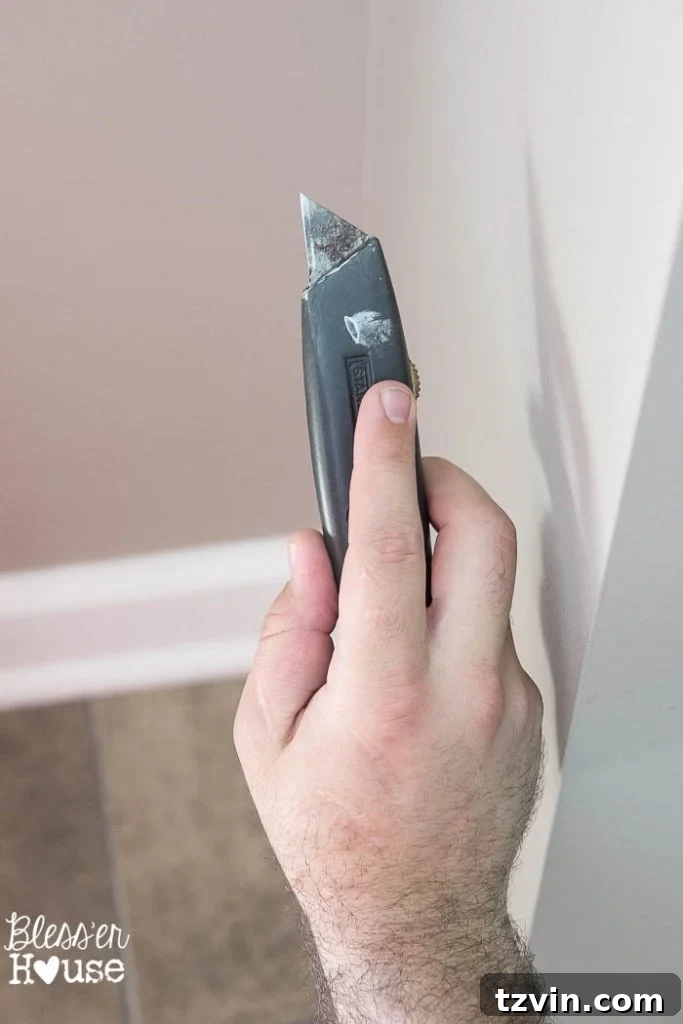 Using a sharp box cutter to carefully score the caulk line where the baseboard meets the wall, preventing drywall damage during removal.