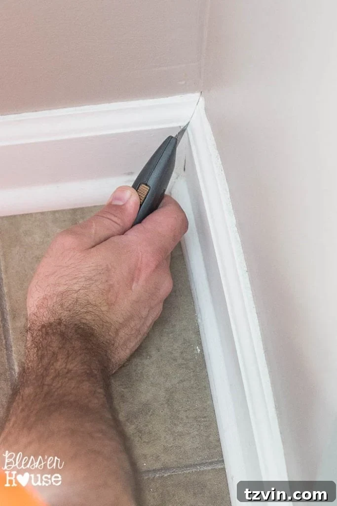 Close-up of scoring the caulk where quarter round meets the baseboard and the floor for clean trim removal.