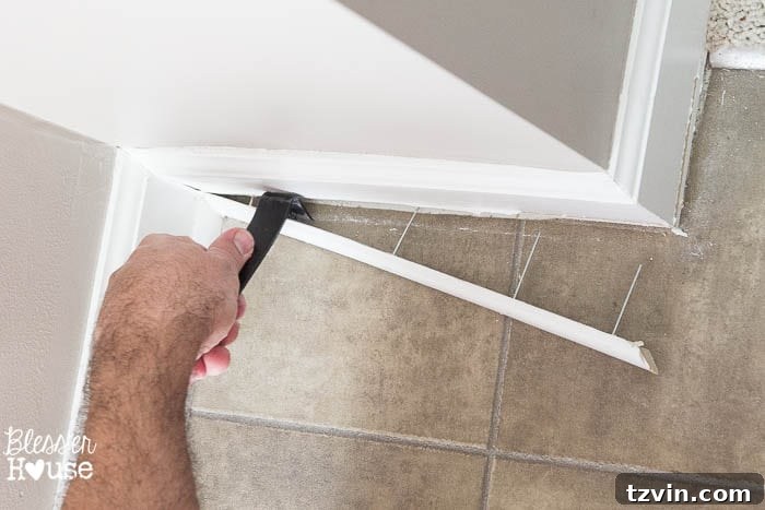 Carefully prying the quarter round molding away from the baseboard with a pry bar, working slowly to prevent damage.