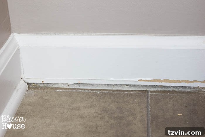 Robert cutting the caulk line where the baseboard meets the wall with a box cutter to prepare for removal.