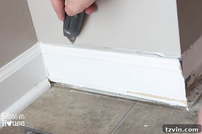 Close-up of the box cutter making a clean cut along the caulk line between the baseboard and the wall.