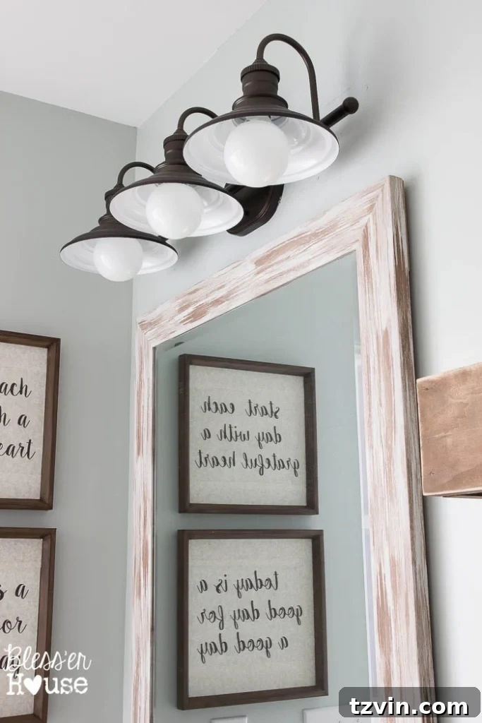 Full view of the modern farmhouse bathroom vanity area, showcasing the mirror, updated light fixture, and white towels.