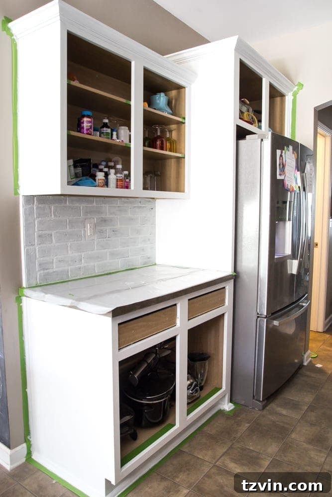 Elevate Your Kitchen: Pro Strategies for Cabinet Painting 11 A kitchen scene with cabinet frames freshly painted white, showing painter's tape still in place and a protected countertop, amidst a DIY kitchen renovation.