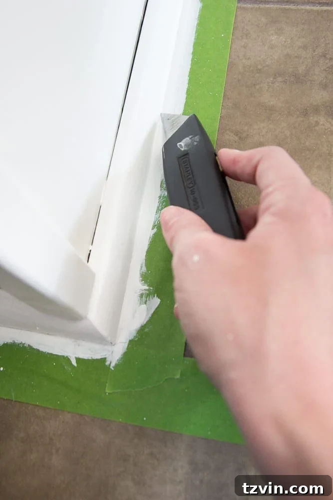 Elevate Your Kitchen: Pro Strategies for Cabinet Painting 12 A close-up of a hand using a utility knife to score painter's tape along a freshly painted kitchen cabinet frame, preventing paint peeling upon removal.