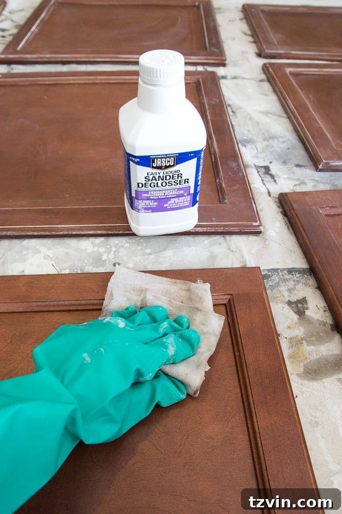 Elevate Your Kitchen: Pro Strategies for Cabinet Painting 7 A person in rubber gloves wiping down a kitchen cabinet door with a deglosser, preparing the surface for priming and painting without sanding.