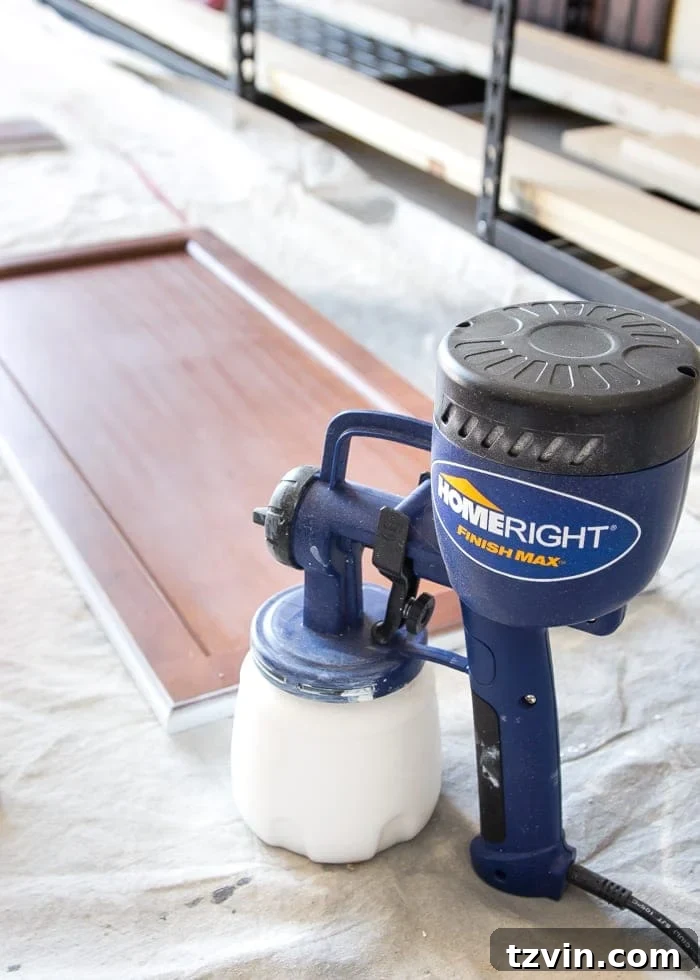 Elevate Your Kitchen: Pro Strategies for Cabinet Painting 8 A close-up view of a hand painting a kitchen cabinet door with a primer using a paint sprayer, emphasizing an even and consistent application for a durable finish.