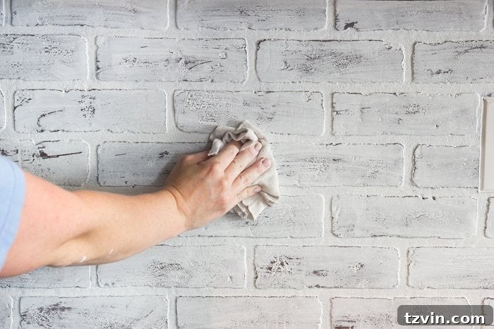 Distressing the whitewash on a faux brick backsplash with a damp rag to achieve a rustic, weathered look