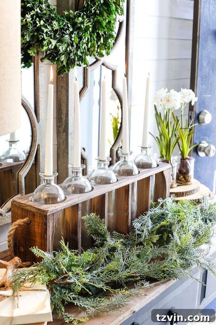 An inviting winter foyer setup, showcasing the soft glow of candles in a decorative vase runner, alongside a stylish lamp and winter greenery, contributing to a warm ambiance.