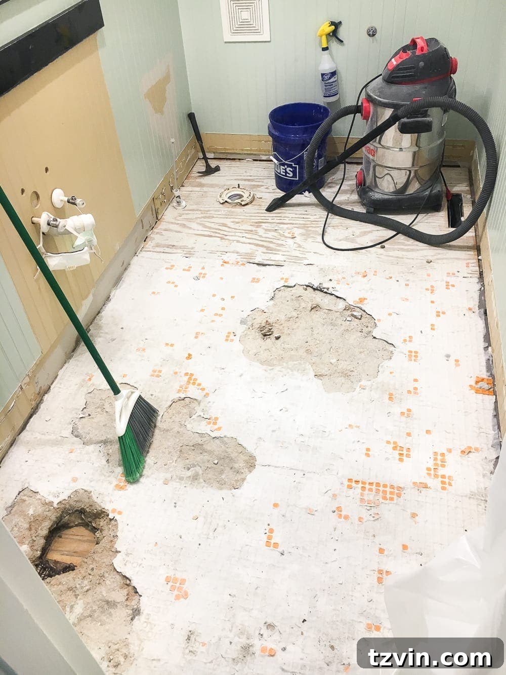 Powder Room Radiance: Faux Marble Tile Floor Upgrade 3 Contractor beginning the demolition of the old travertine floor in the powder room, revealing the subfloor beneath. This image shows the early stages of the bathroom renovation project.