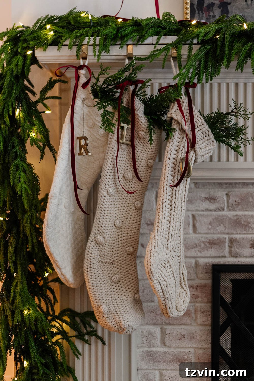 Two cozy Christmas stockings, one red and one white, hanging on a rustic wooden mantelpiece adorned with a bright red ribbon, pinecones, and green foliage, exuding a warm holiday charm.