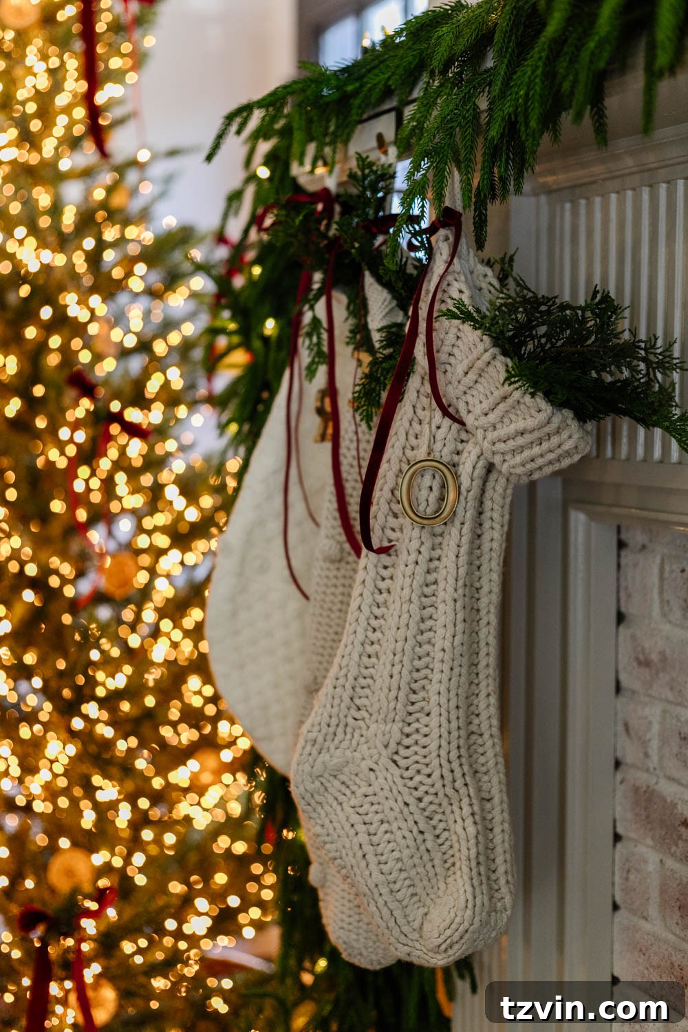 Close-up of three festive Christmas stockings, red, green, and white, hanging on a rustic wooden mantelpiece adorned with a bright red ribbon and natural foliage, evoking a cozy holiday atmosphere.