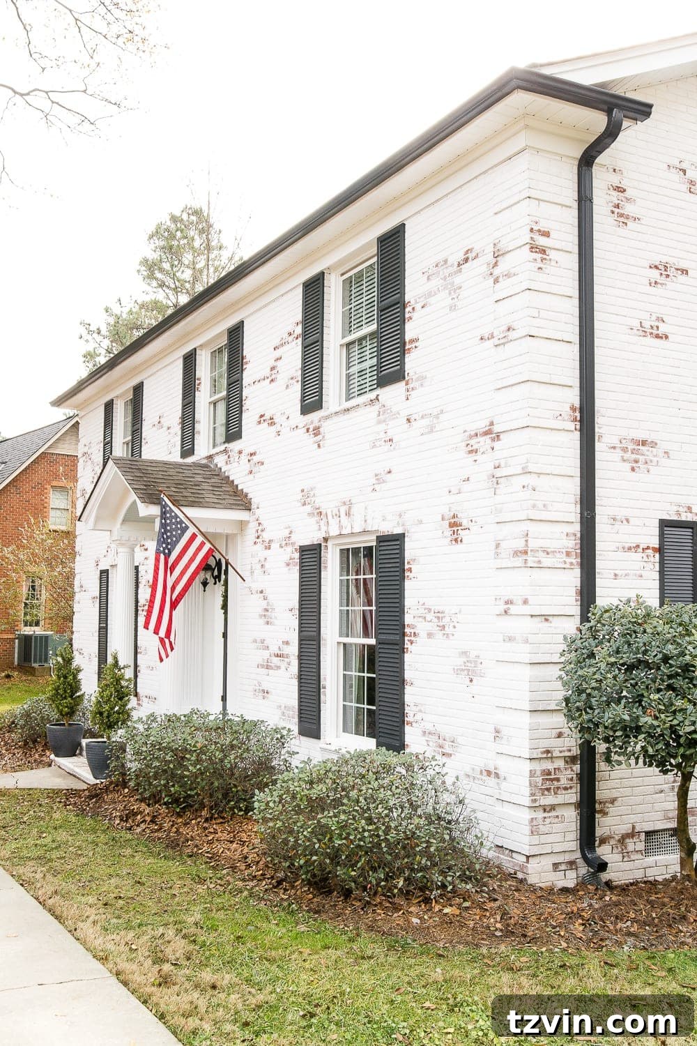 white brick colonial house with black shutters and black gutters