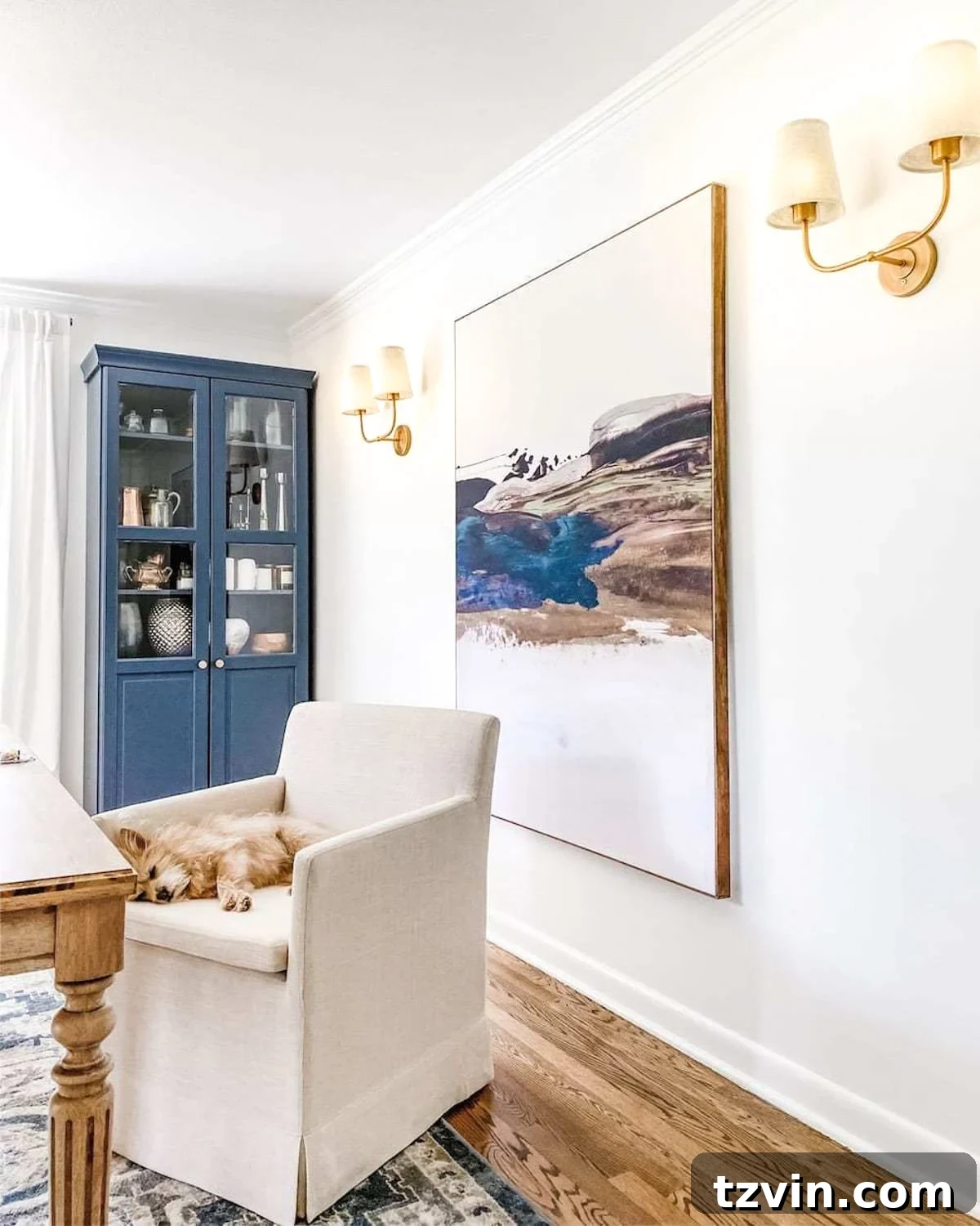 Stylish double-shaded vintage wall sconces illuminating a home office featuring oversized art, a rolling chair, and a striking navy cabinet.