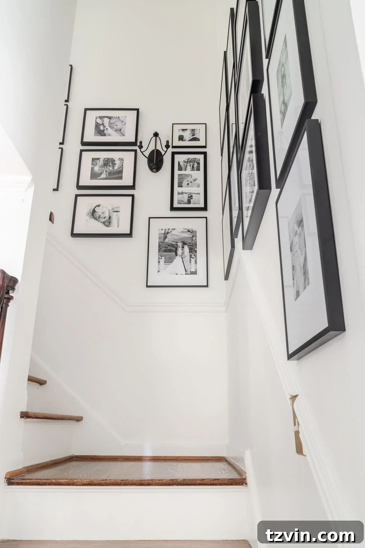 Dramatic black candelabra sconce serving as a focal point on a family gallery wall alongside a winding staircase.