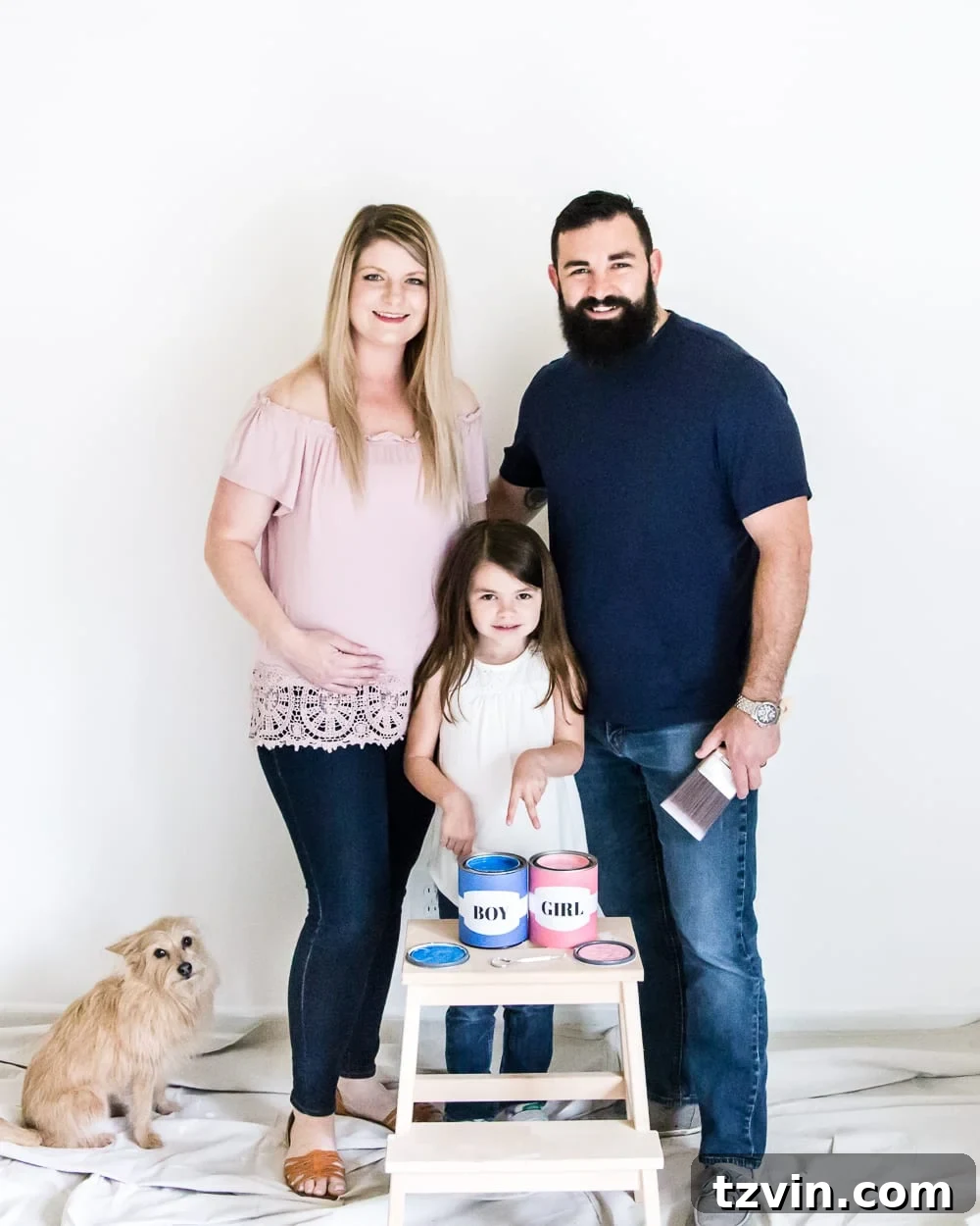 Our Budding Baby Reveal 4 The couple smiles expectantly during their gender reveal photoshoot in the nursery, holding paint trays and looking at each other.