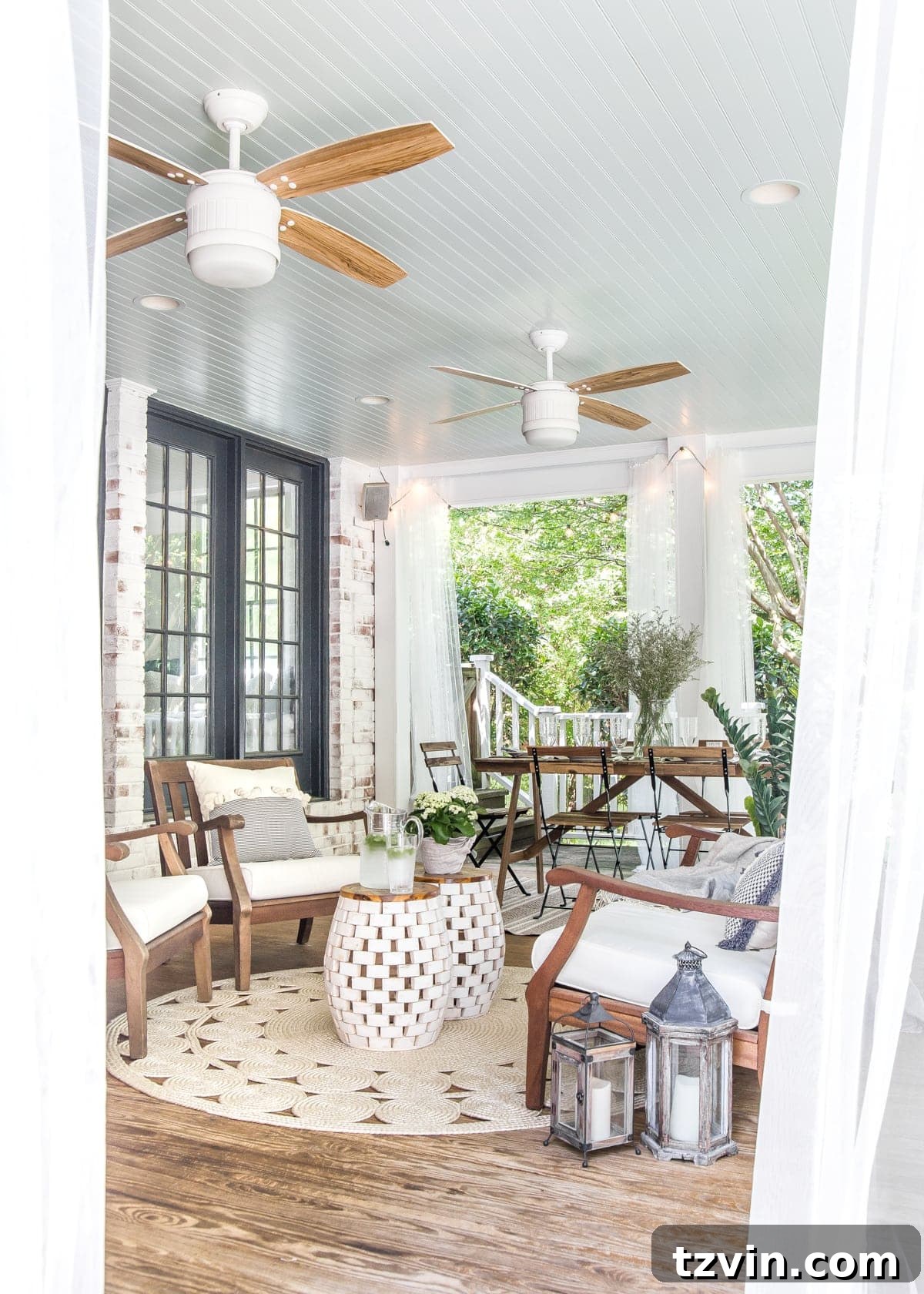A beautifully decorated back porch ready for summer, featuring comfortable seating, string lights, and sheer curtains.