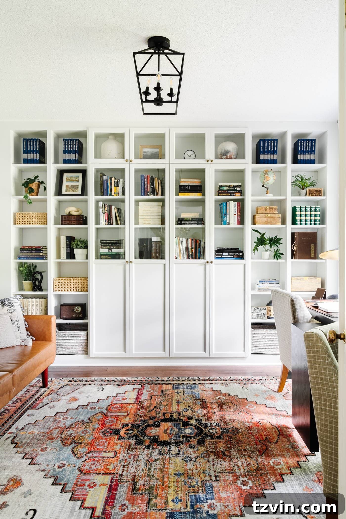 23 Smart Hacks to Make Your Small Room Feel Instantly Bigger 13 home office with white built-in bookshelves and glass front cabinets, futon, rug, and desk against a window