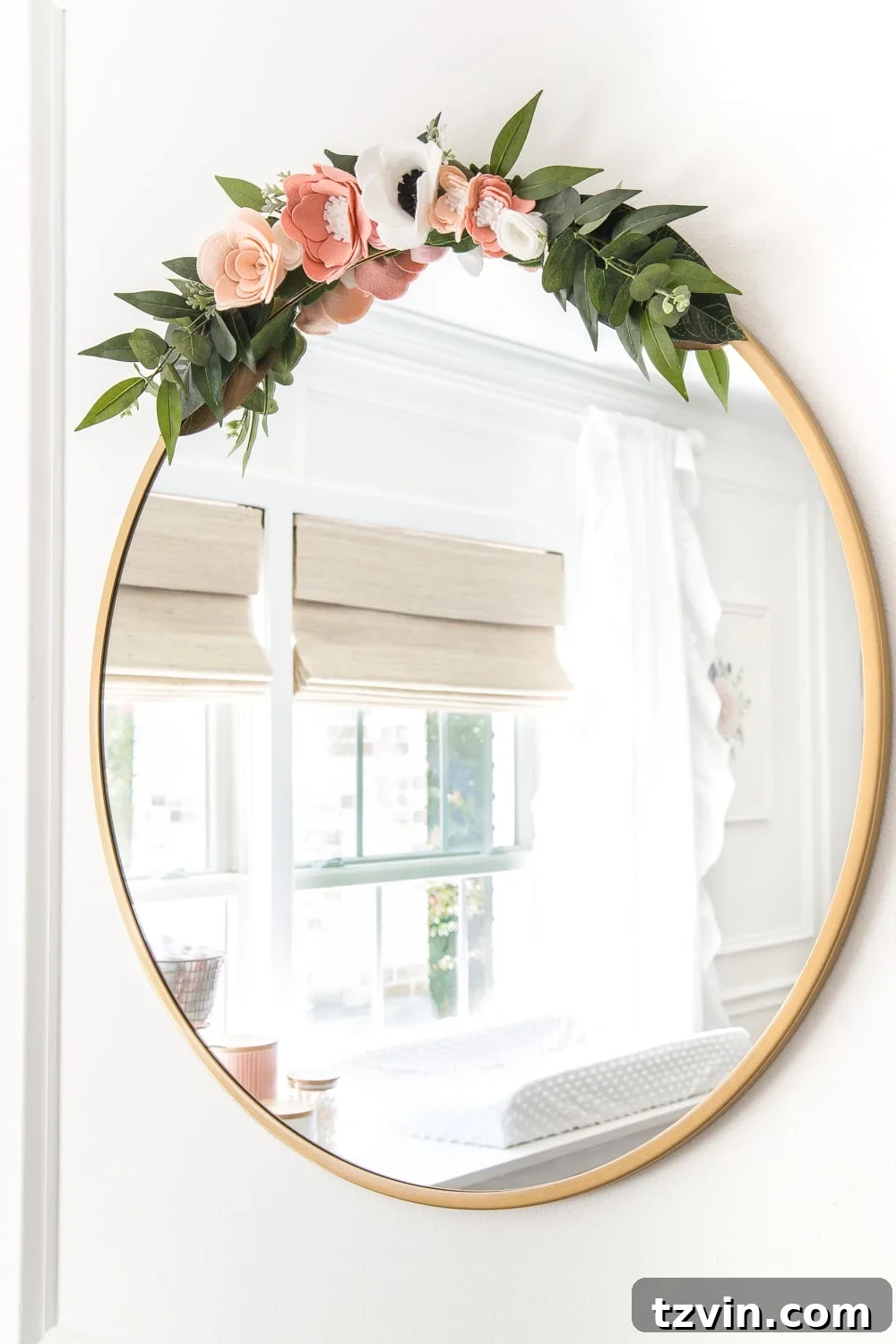 Blossoming Dreams: White Floral Nursery Reveal 23 Round mirror with a small felt flower swag in the white nursery.