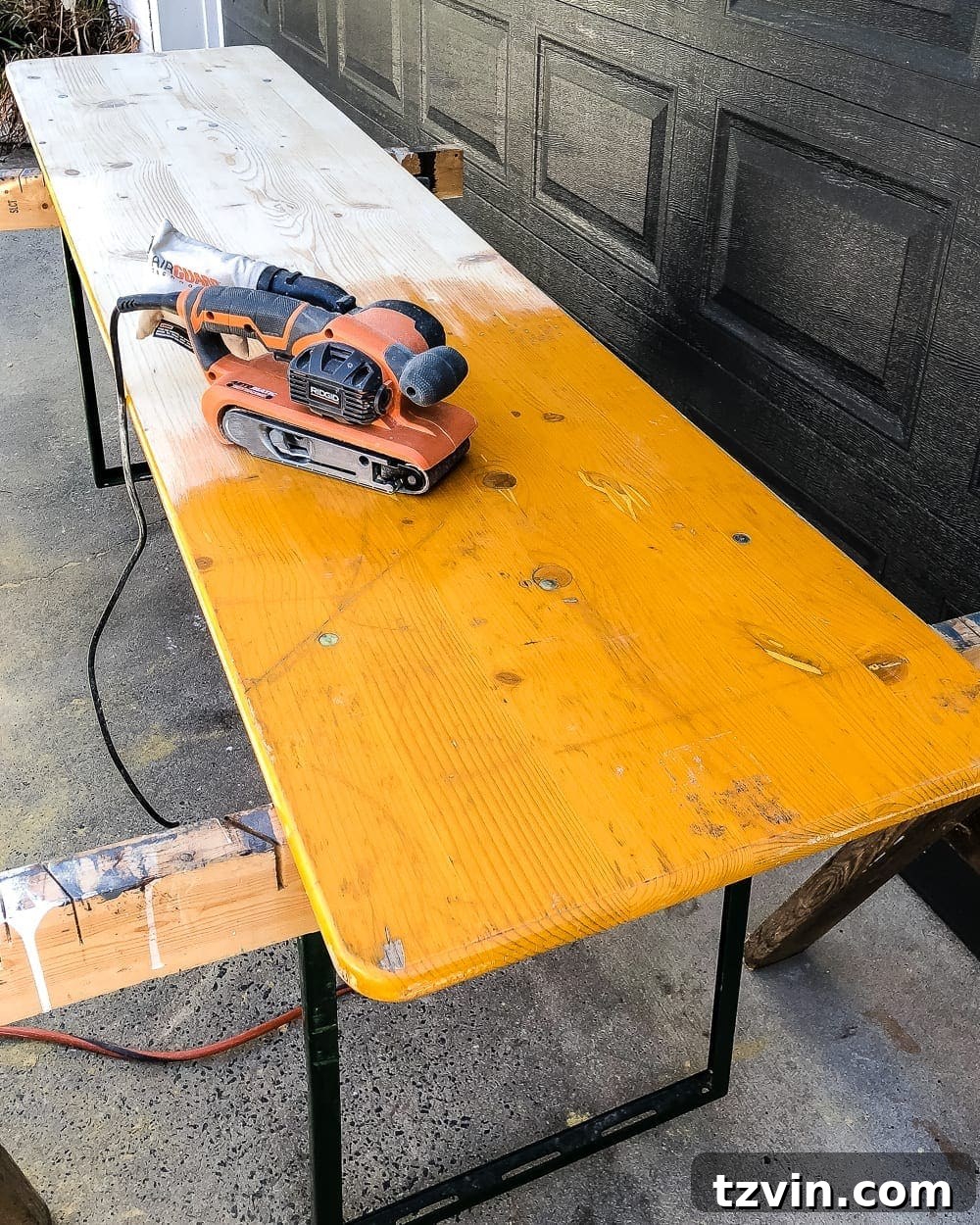 Mid-process shot of refinishing an antique beer garden table, showing one bench sanded and ready for stain, beside the original finish.