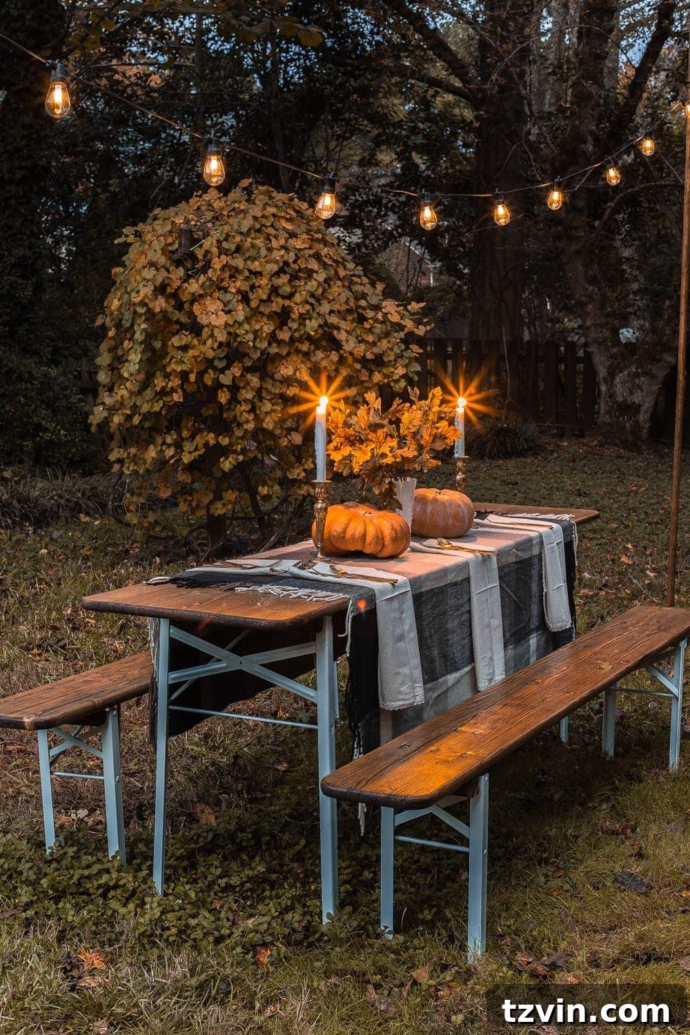 Beer garden table with string lights for fall evening gatherings, decorated with pumpkins and candles.