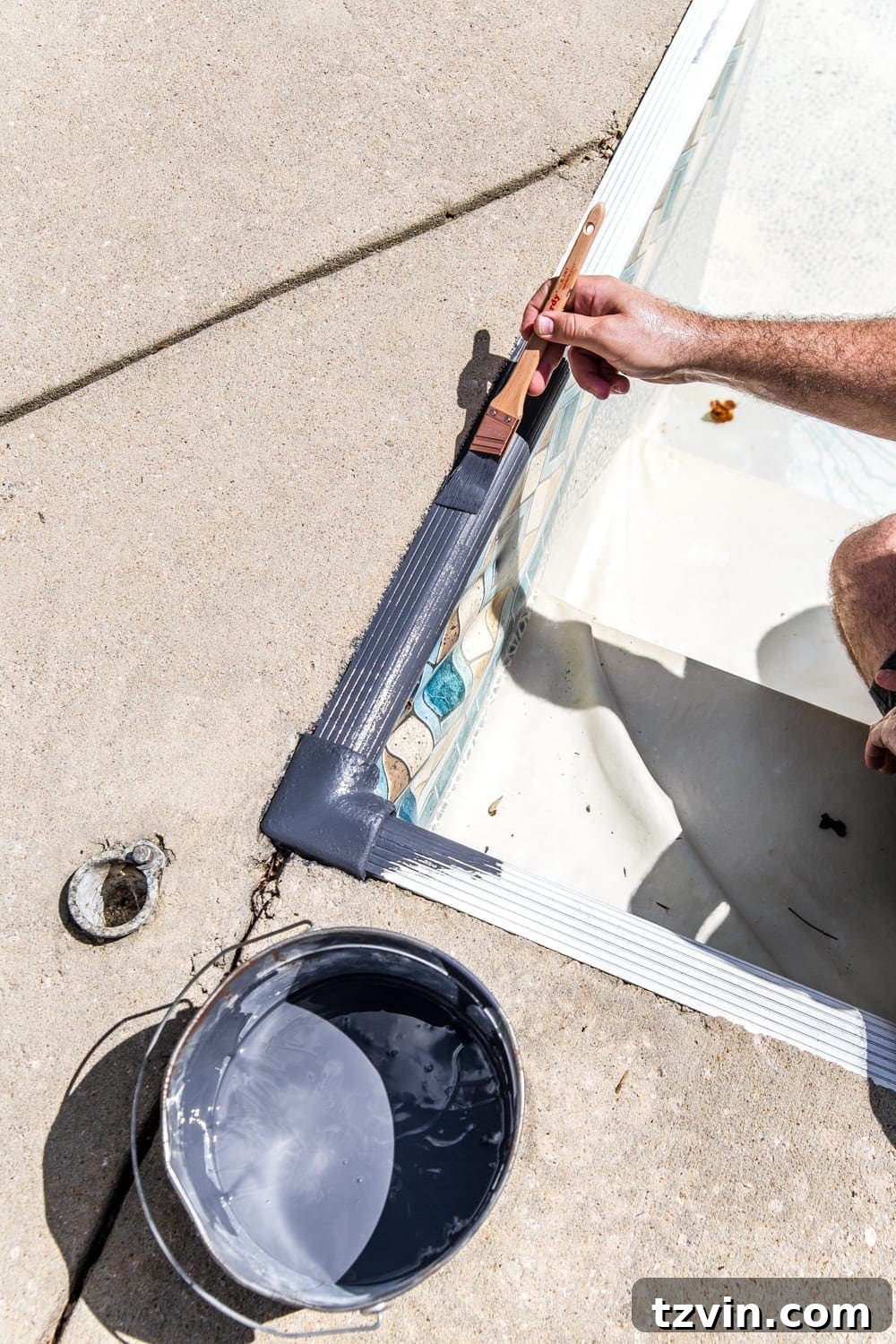 Robert painting the pool coping strip in a dark gray to match the new liner