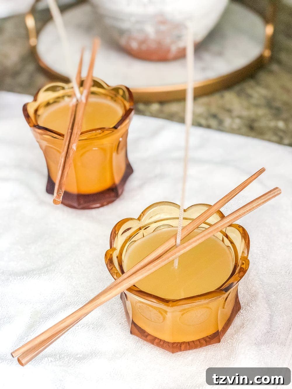 Candle wicks stabilized with chopsticks as soy wax cools in repurposed dishes for DIY candle making