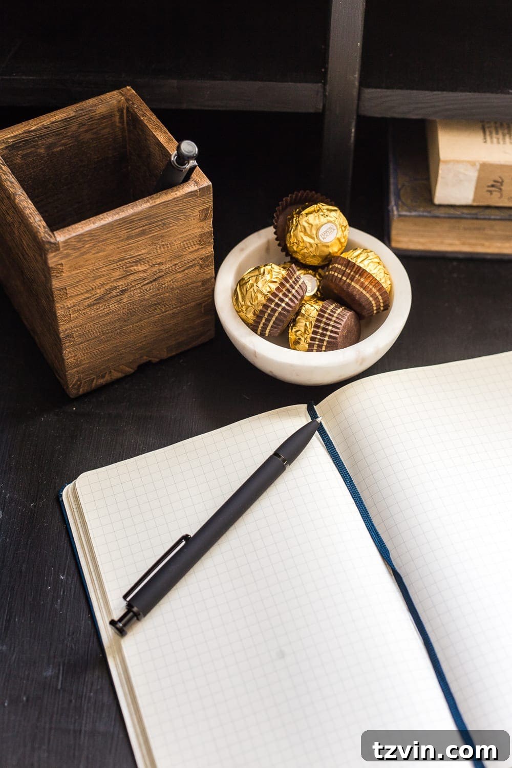 A notepad, pen, and a small dish of chocolates on a bedside table, offering delightful and practical amenities for guests.