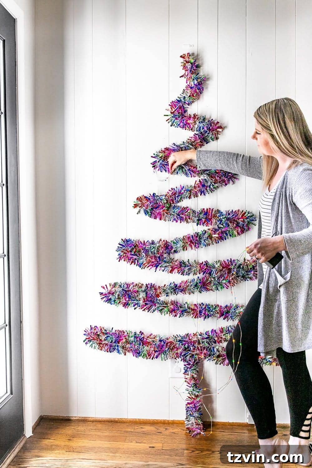 Adding string lights to an already formed garland wall Christmas tree for illumination.