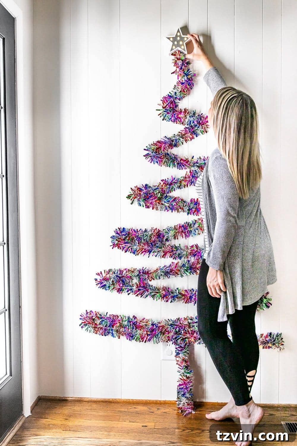 Attaching a star topper to the peak of a wall-mounted garland Christmas tree.