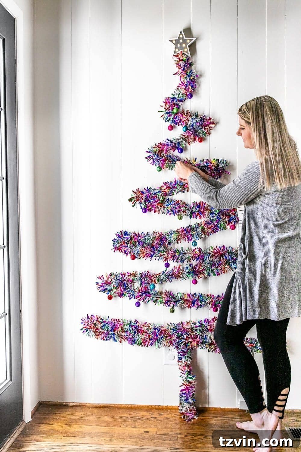 Decorating a wall Christmas tree with various small ornaments, enhancing its festive appearance.