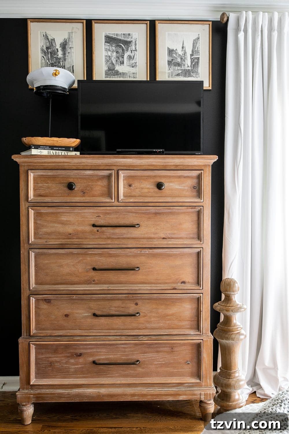 Moody Modern Vintage Master Bedroom Transformation 10 Bedroom TV disguised on dresser top with black paint background, flanked by vintage cityscape sketches and a sentimental hat display.