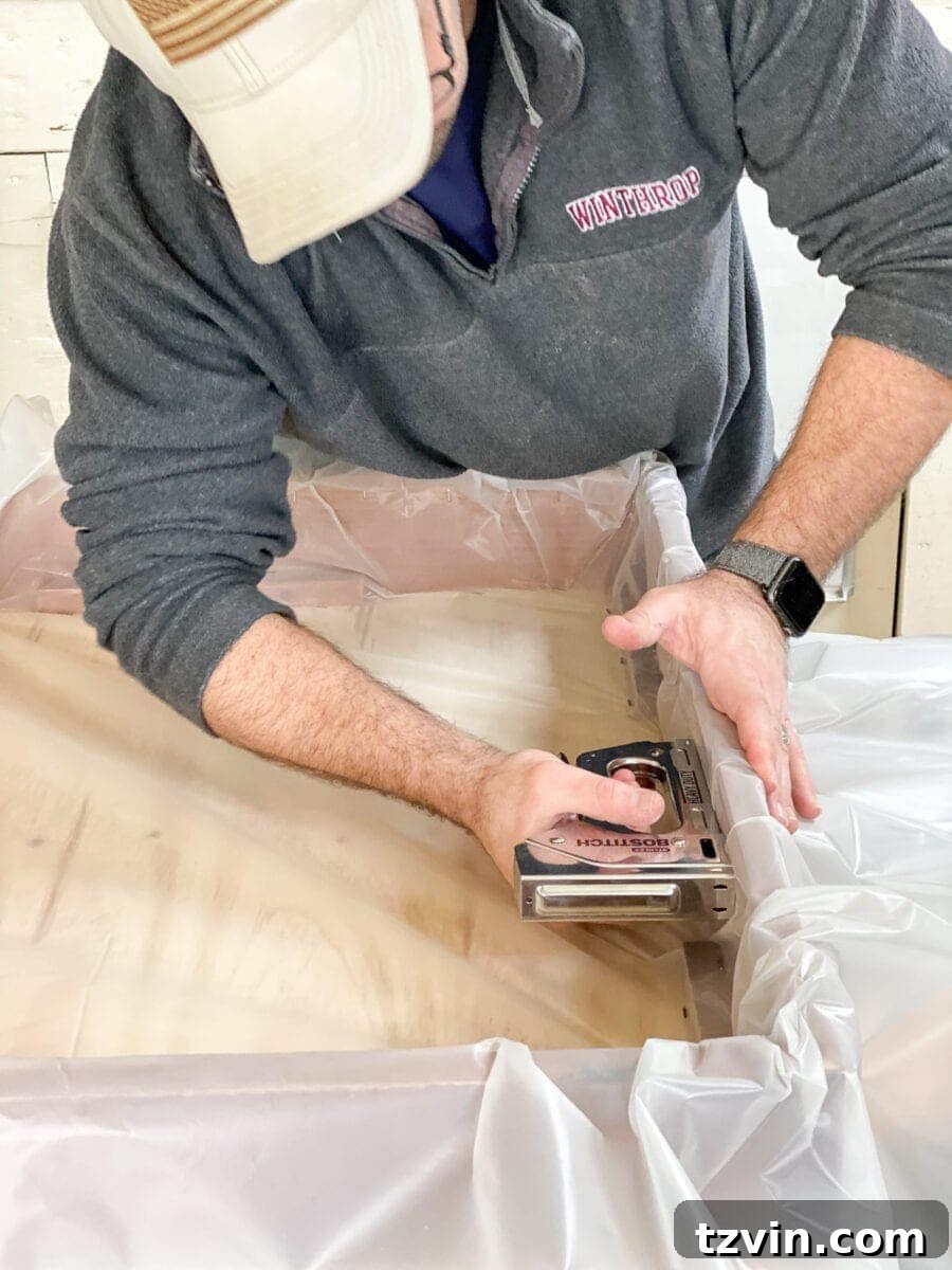 Stapling the plastic drop cloth securely inside the wooden planter box