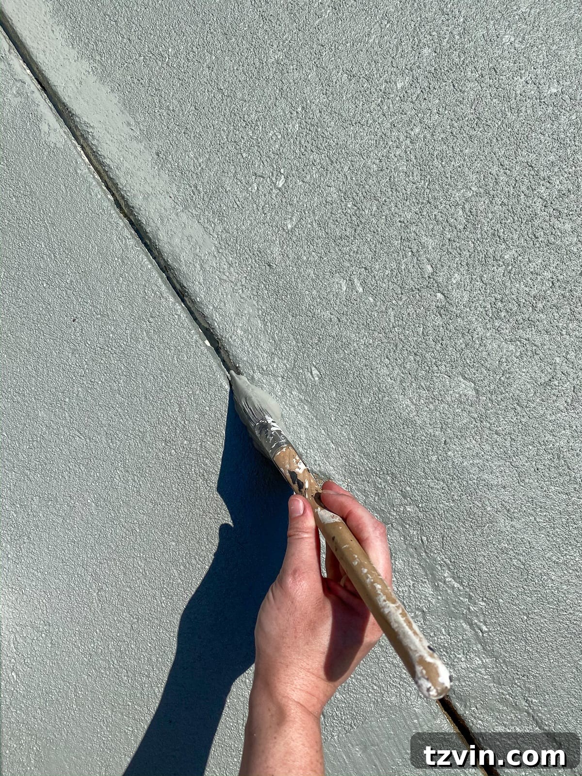 applying concrete paint in cracks and edges to finish a patio