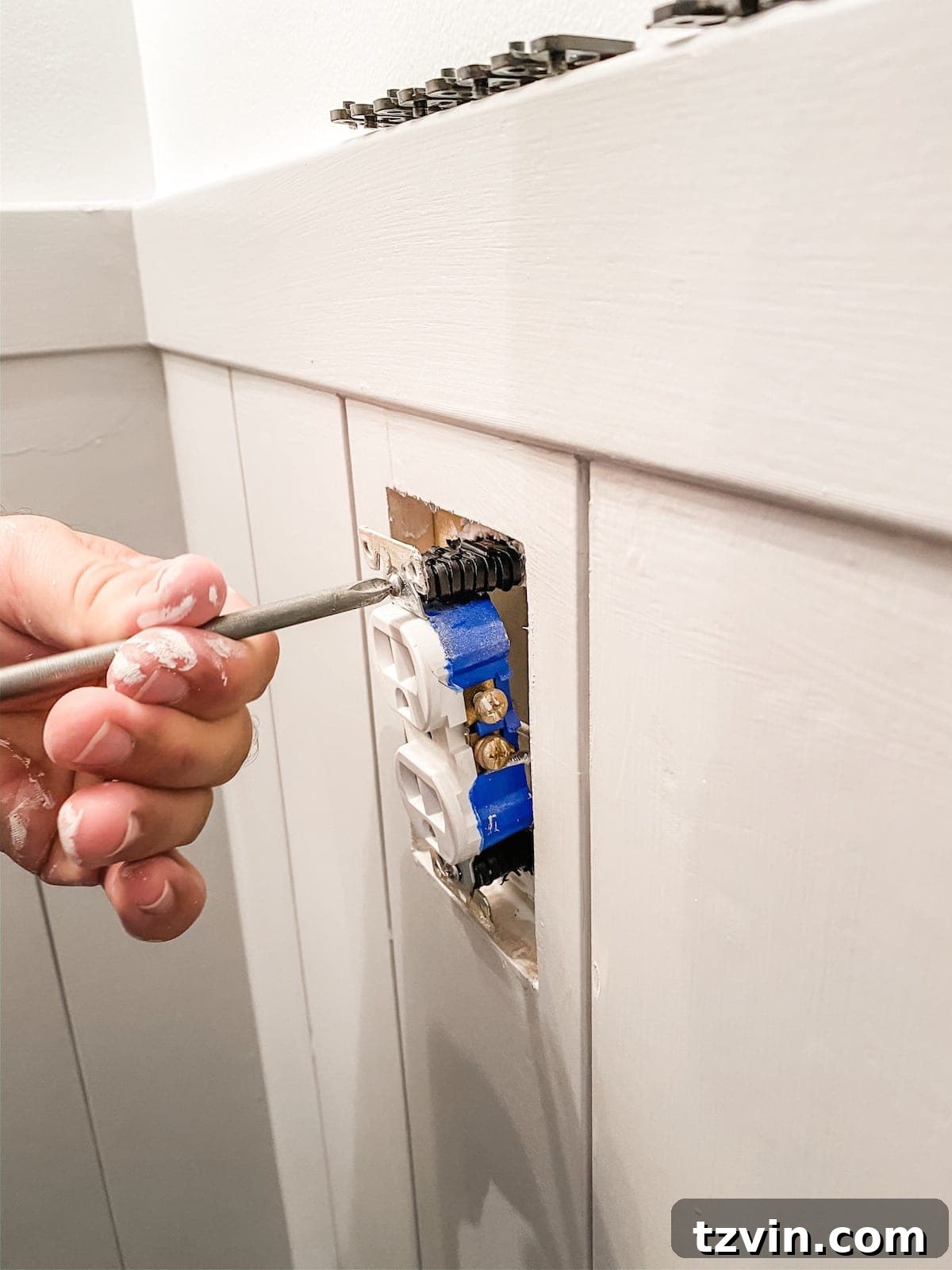A close-up of an electrical outlet being brought flush with newly installed shiplap wainscoting using outlet spacers, ensuring a safe and finished look.