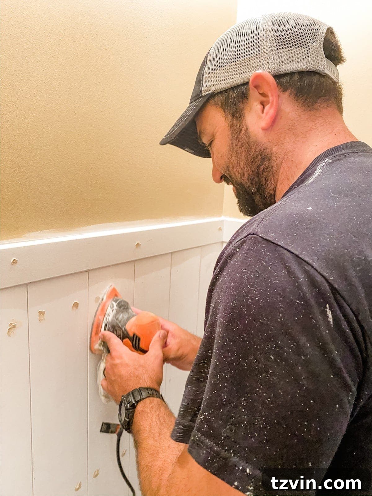 A close-up shot of a hand sanding wood filler on vertical shiplap planks, highlighting the meticulous process of preparing the surface for painting.