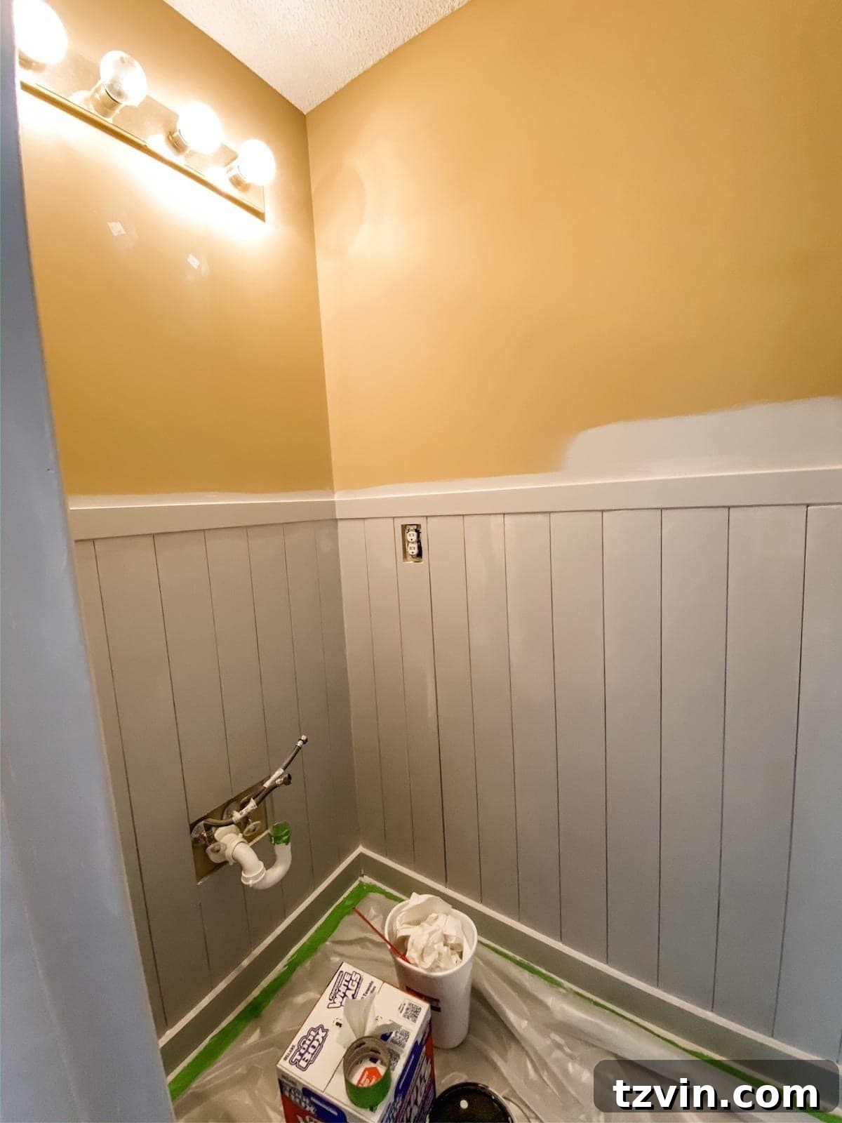 A person meticulously painting the newly installed vertical shiplap wainscoting in a bathroom with a roller, ensuring an even and clean coat.