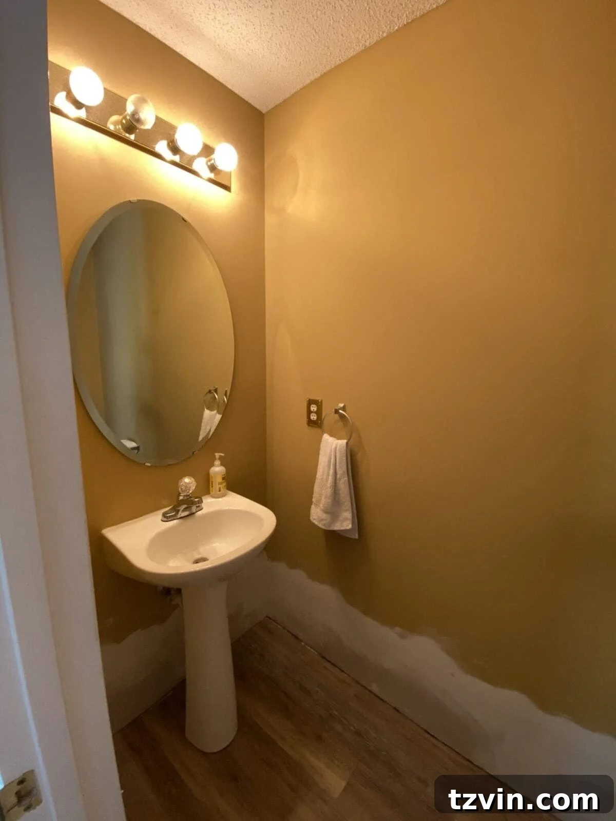 Before shot of a powder room with outdated gold-painted walls, showing a dull and uninspired interior awaiting renovation.