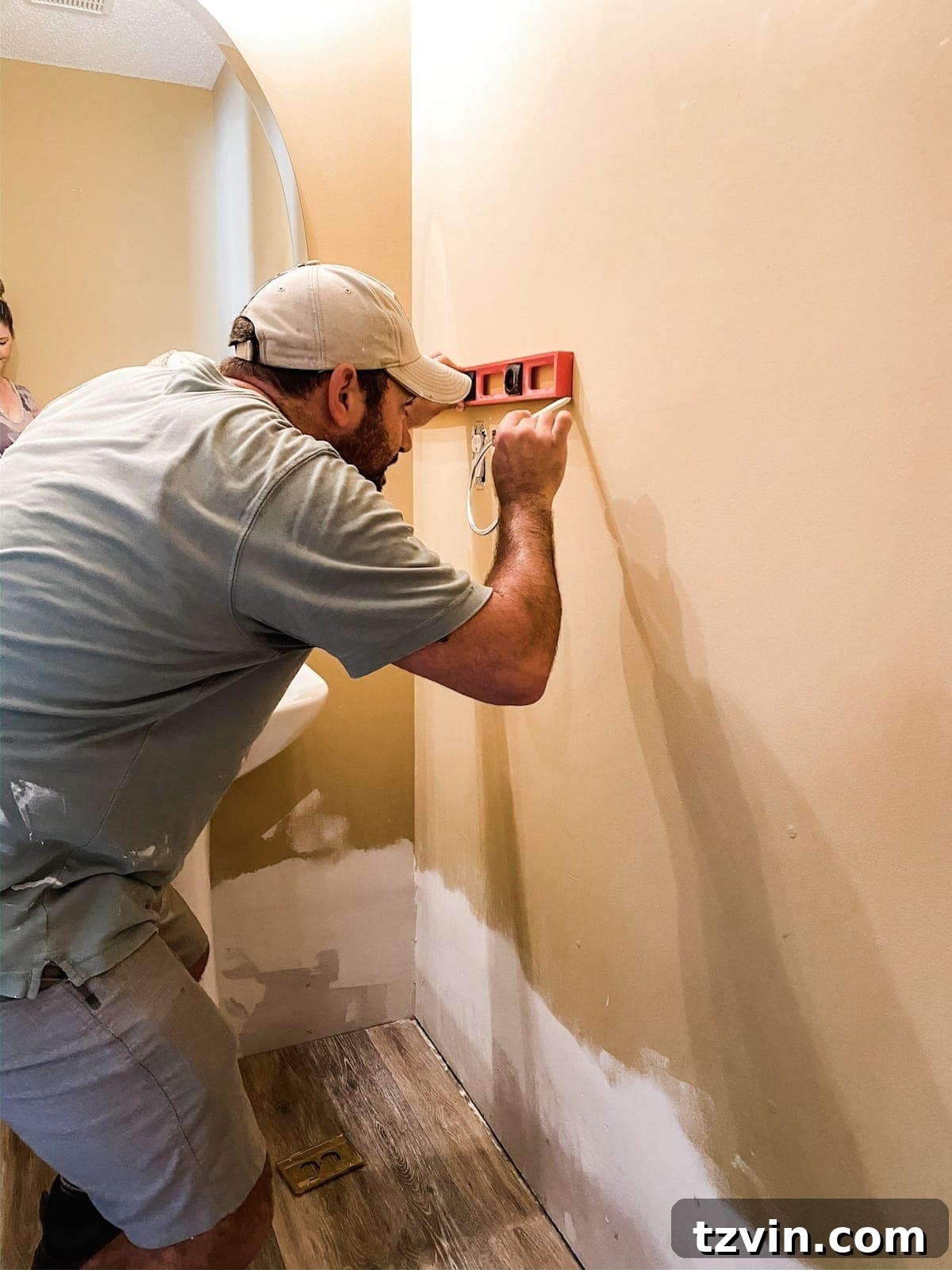 A person using a level and pencil to mark the desired height of the vertical shiplap wainscoting on a wall before installation, ensuring a straight guide line.