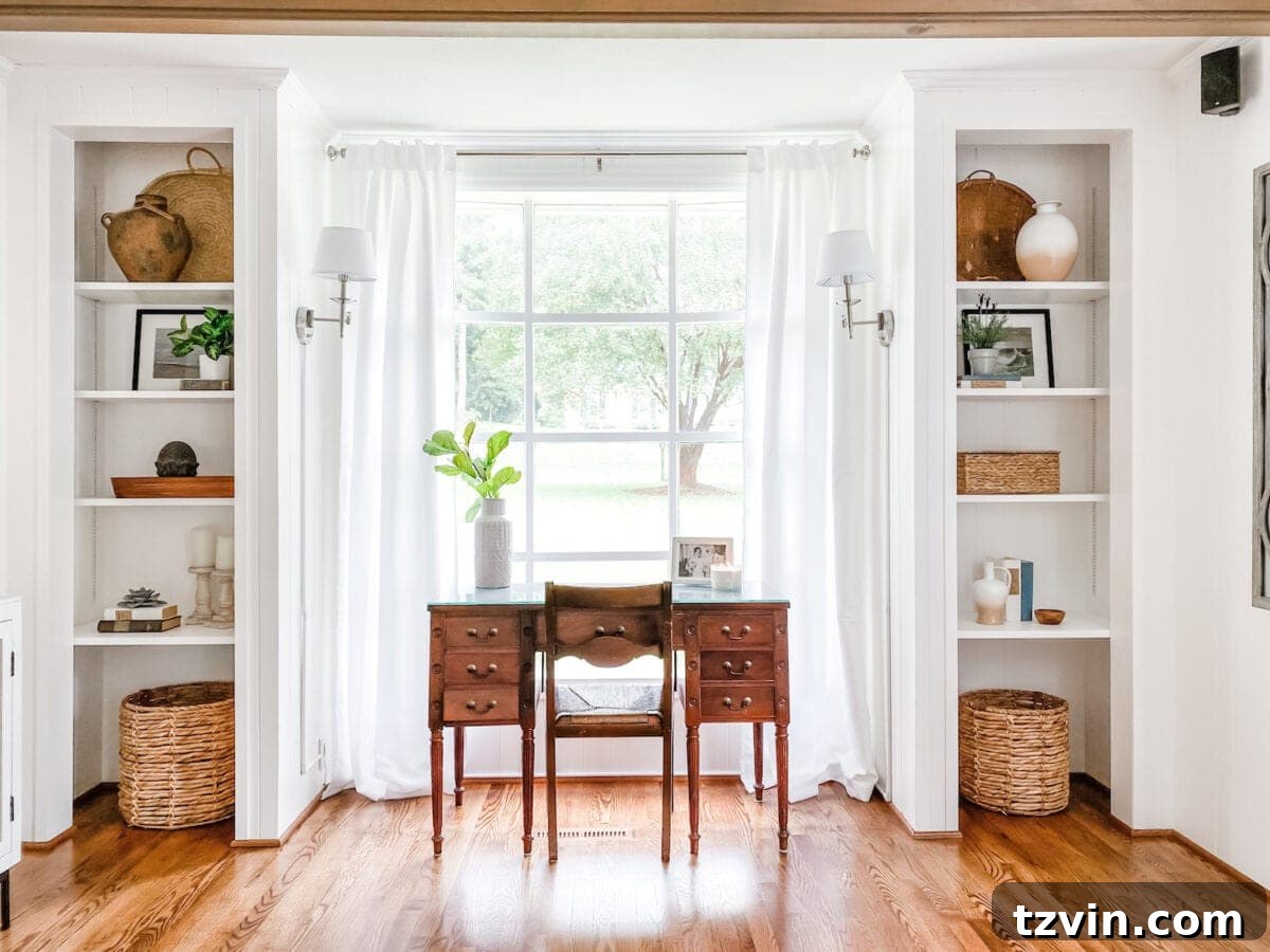Bright white living room office with custom built-in shelves and a desk in front of a window
