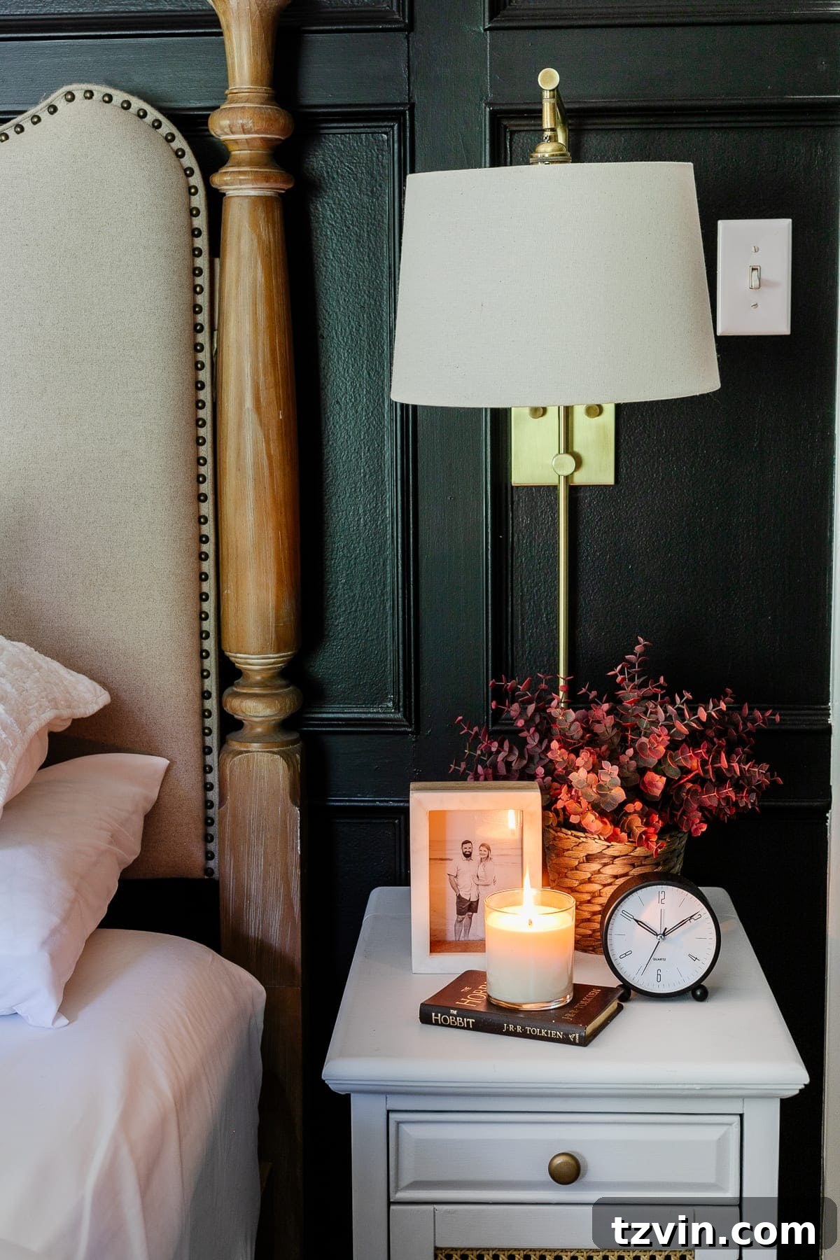 Cozy fall decor on a bedroom nightstand, featuring warm-toned artificial plants and a lit candle.