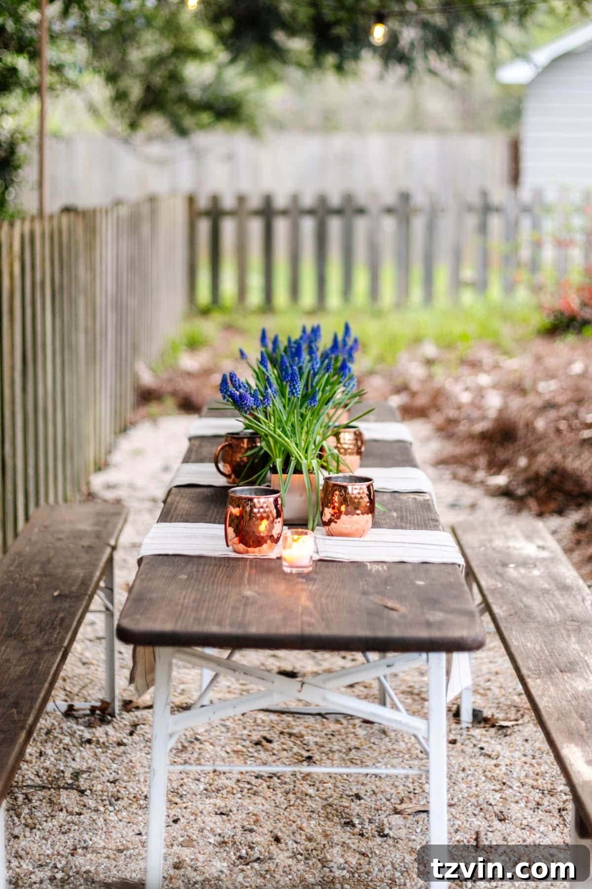 Summer table decor on a beer garden table set for a backyard cookout, featuring fresh flowers and ambient lighting.