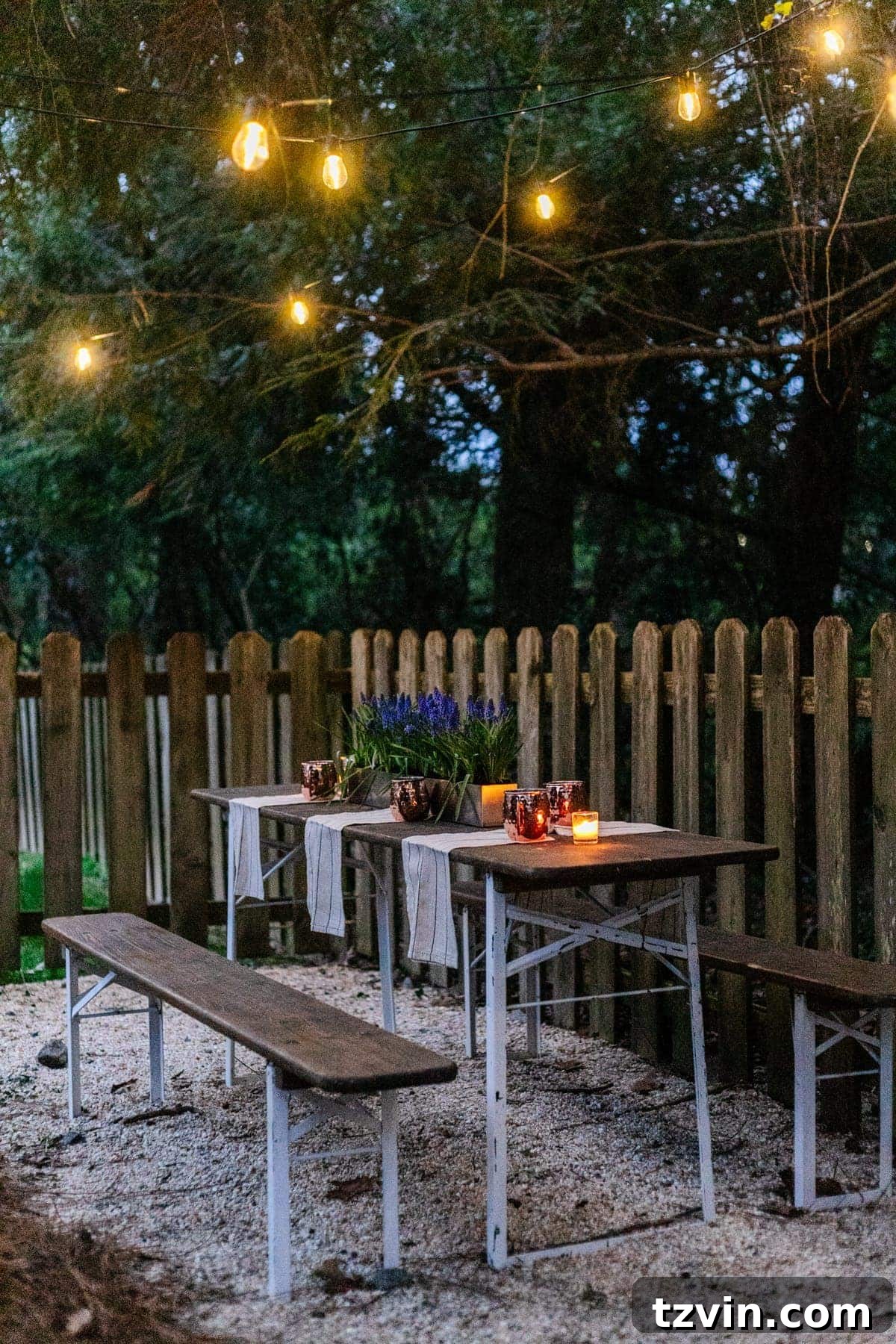 An inexpensive backyard patio area created with a folding table, string lights, and pea gravel, radiating a cozy ambiance.