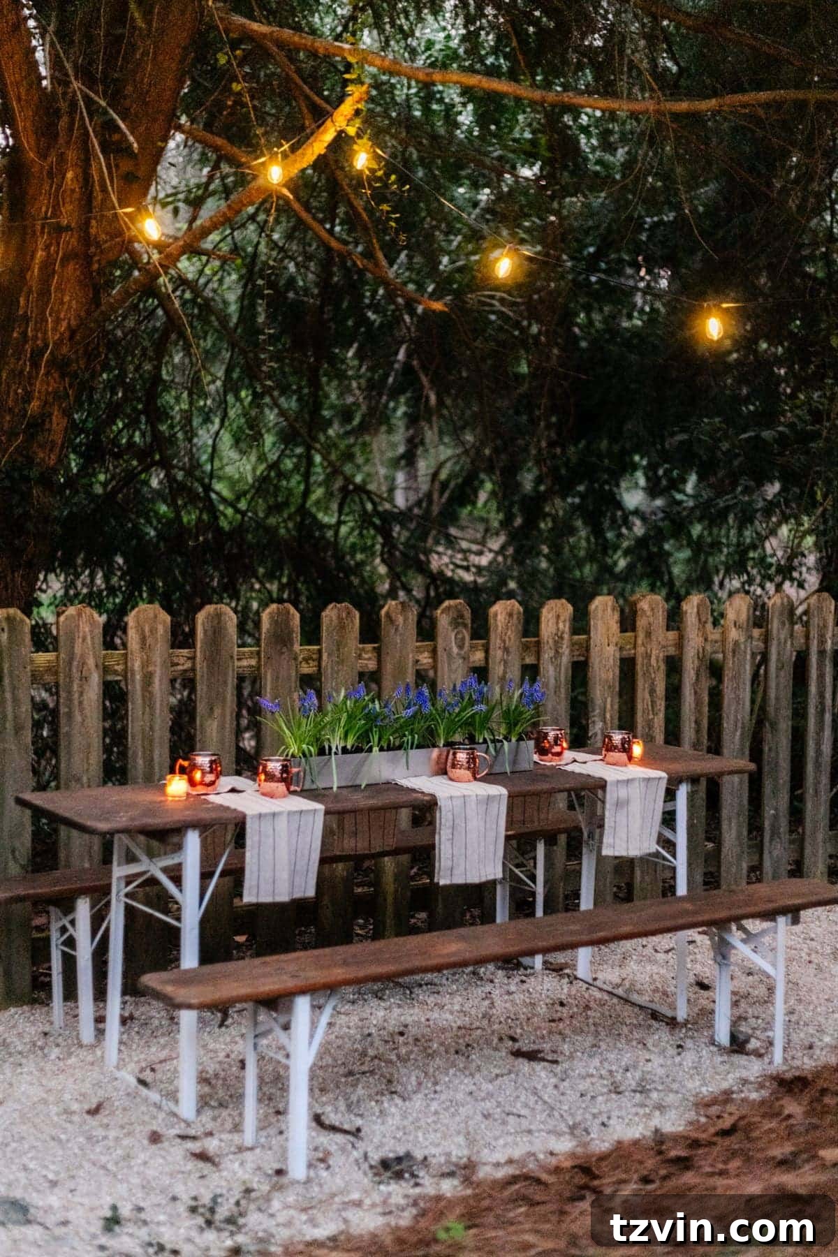 Hanging solar string lights in trees above a folding table to define a charming backyard beer garden dining area at dusk.