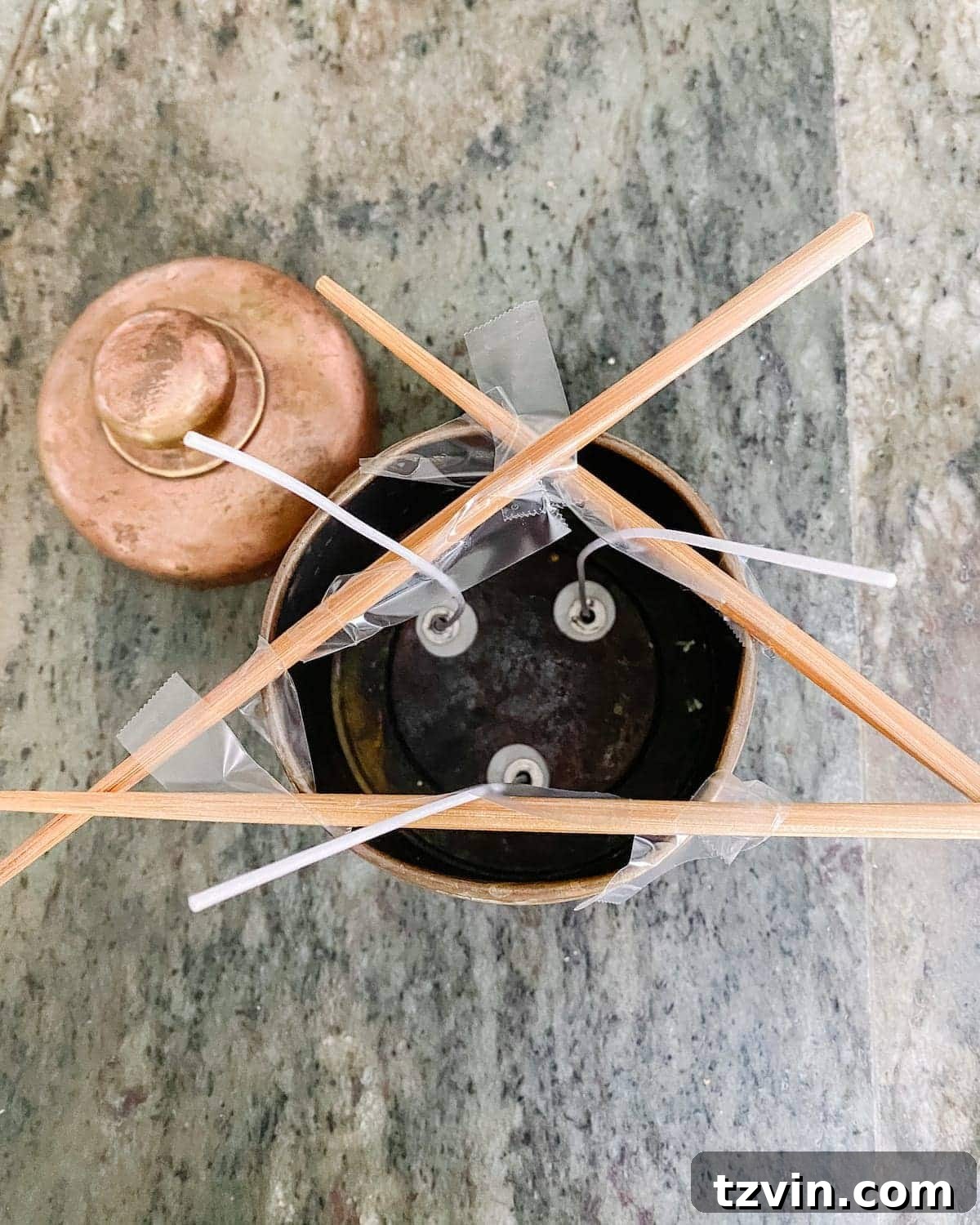 A candle wick held upright and centered by a wick holder across a brass canister, ready for wax pouring.