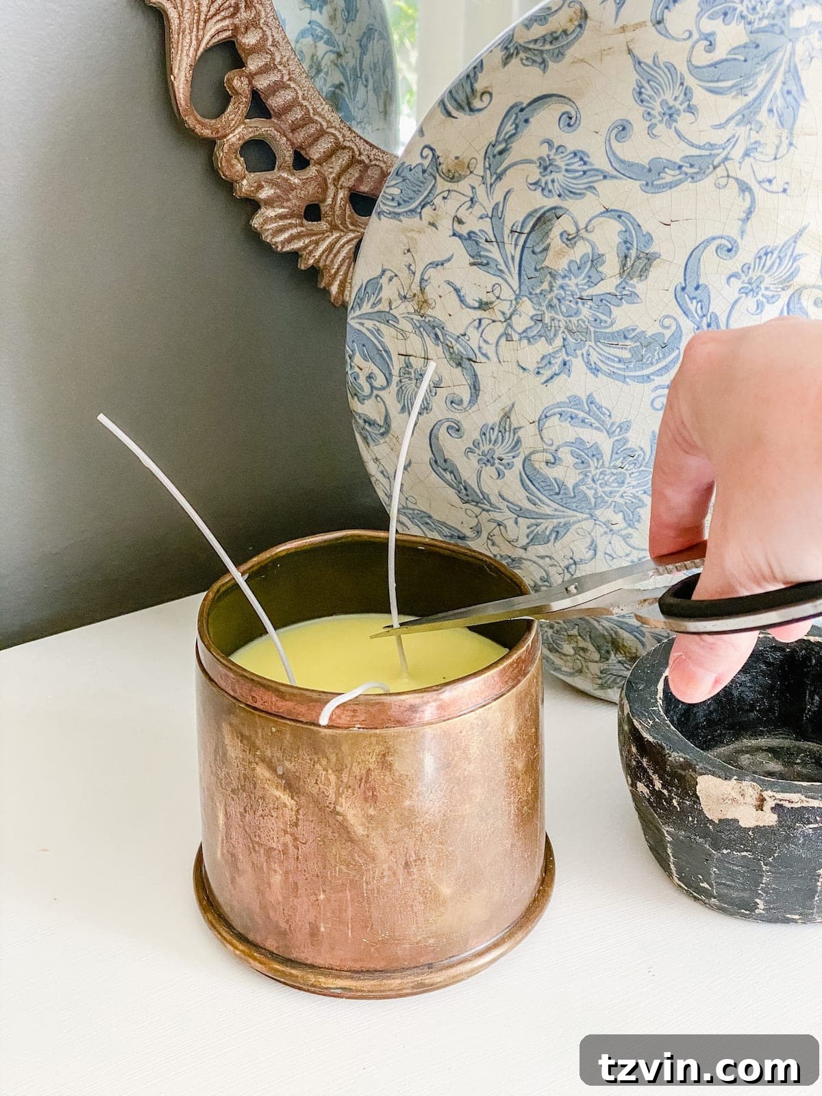 Melted wax being poured into an antique brass canister with a centered wick, creating a DIY candle.