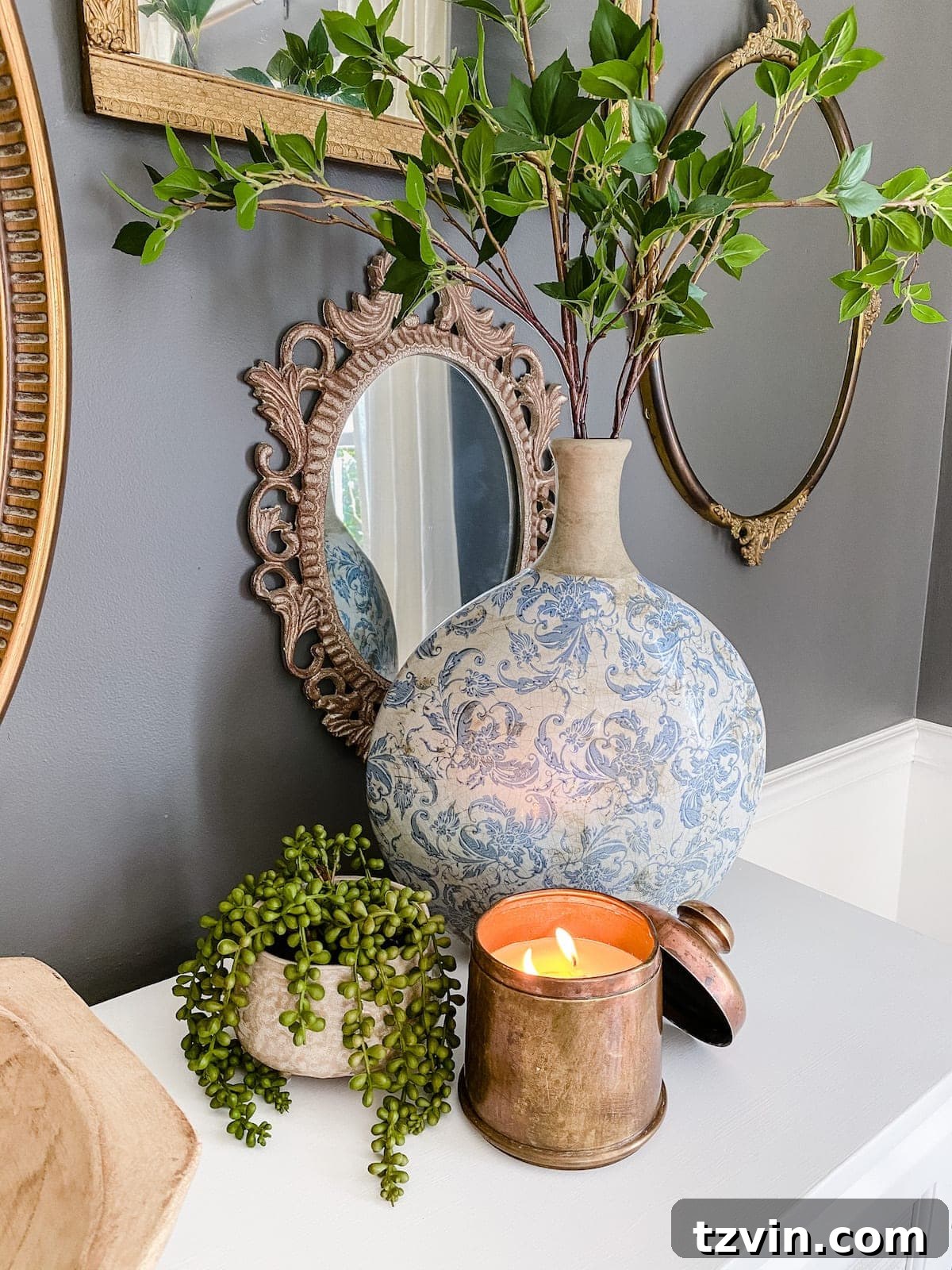 A DIY candle made from an antique brass canister, elegantly displayed with a blue and white Chinoiserie vase and fresh greenery, enhancing home decor.
