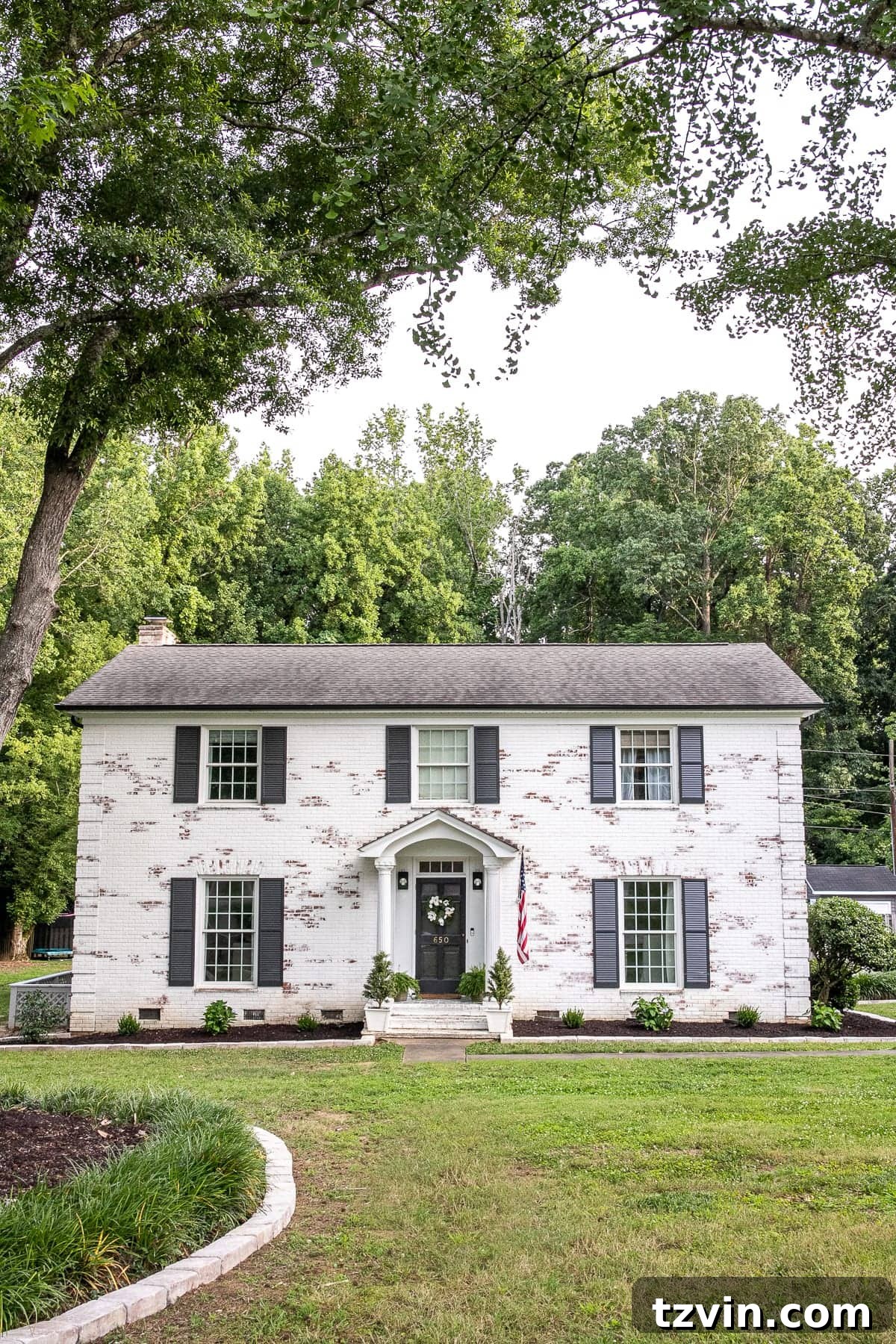 After shot of the house exterior featuring limewashed brick in Romabio Bianco White, fresh landscaping, and updated door colors.