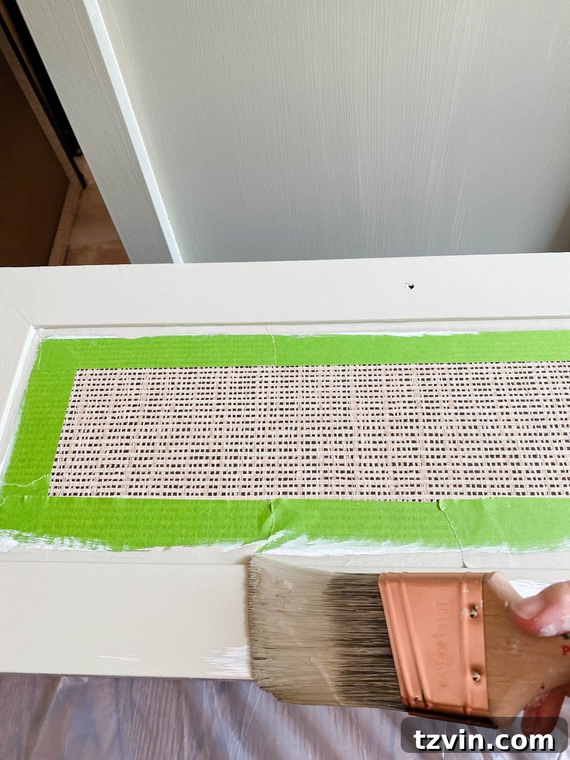 Close-up of a laminate dresser receiving a coat of acrylic paint after being primed, illustrating the painting process.