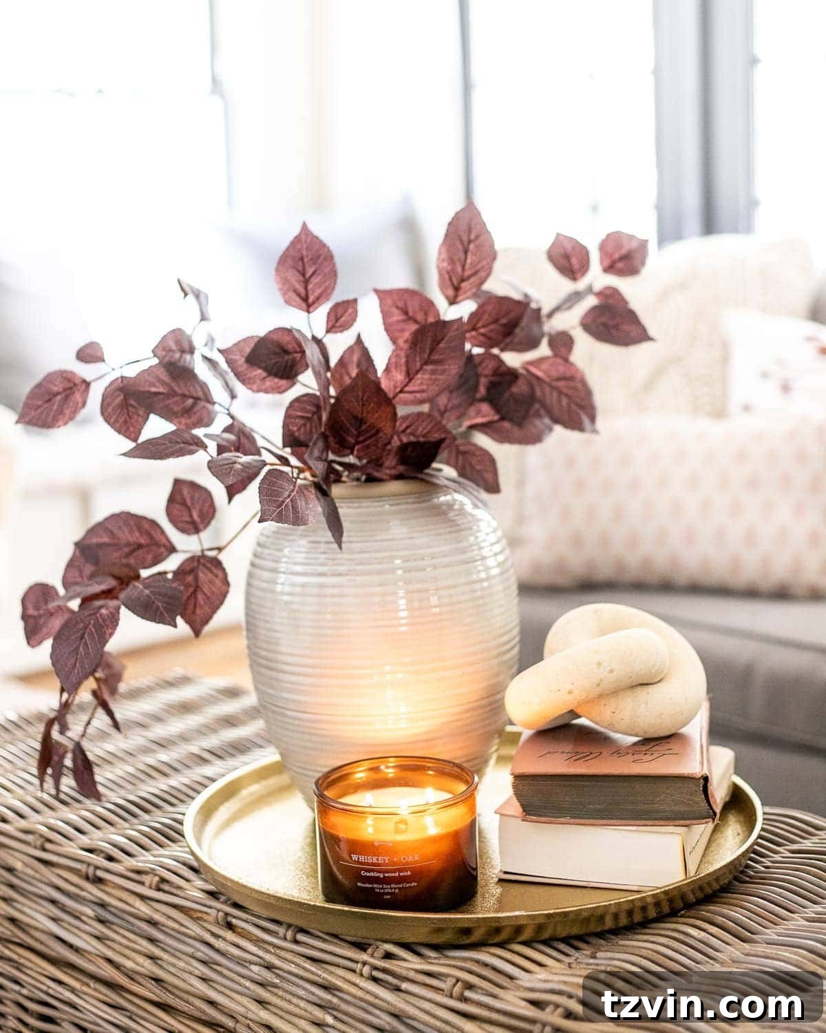 fall decor on a coffee table with brass tray, amber glass candle, wood knot, books, and vase with autumn stems