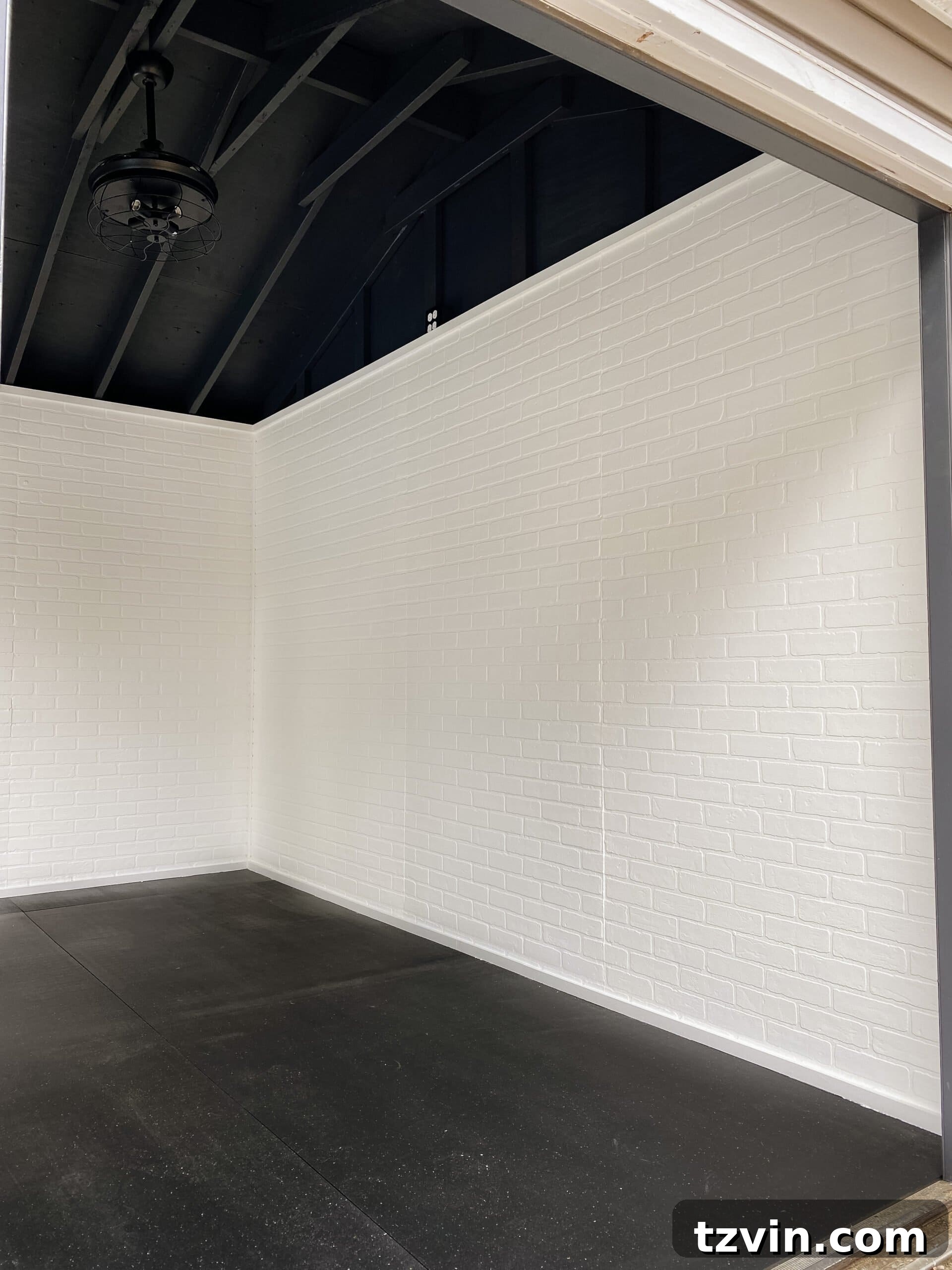 Faux Brick Gym Shed Upgrade 17 Spacious home gym with clean white faux brick wall panels, a black ceiling, and open area awaiting fitness equipment and mirrors.